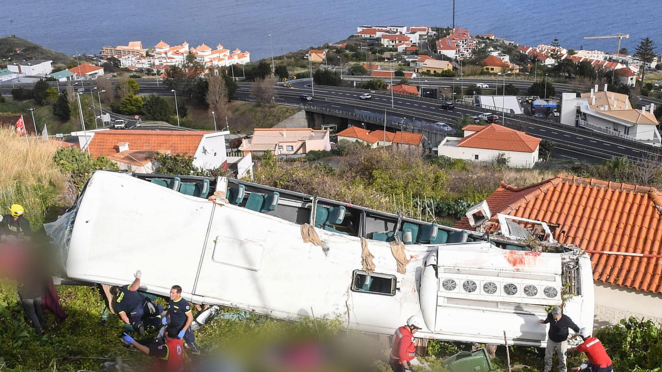 Rettungskräfte stehen nach einem schweren Busunglück auf Madeira an dem Bus: Die Identifizierung der Toten dauert noch an, teilte die örtliche Klinik mit.