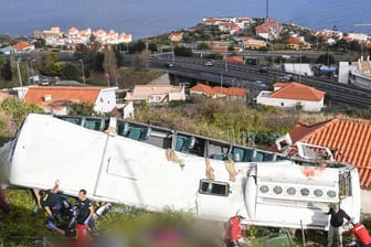 Rettungskräfte stehen nach einem schweren Busunglück auf Madeira an dem Bus: Die Identifizierung der Toten dauert noch an, teilte die örtliche Klinik mit.