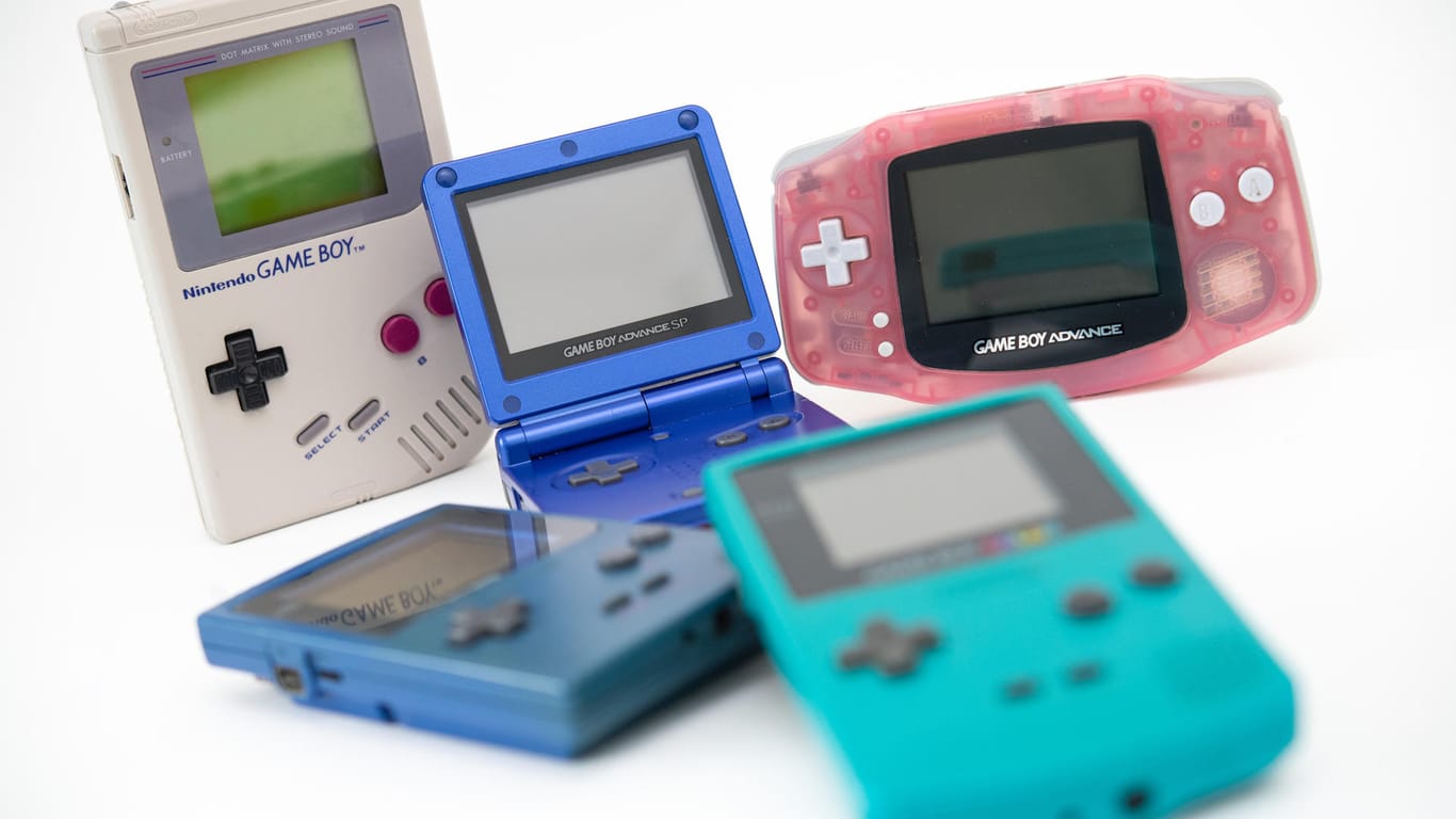Verschieden Game-Boy-Versionen: Der erste Game Boy (l in Grau) erhielt über die Jahre etliche Nachfolger wie den Game Boy Pocket (blau, liegend), den Game Boy Advance SP (Mitte, aufgeklappt), den Game Boy Advance (r, rosa) und den Game Boy Color (vorne, mit Farbdisplay).