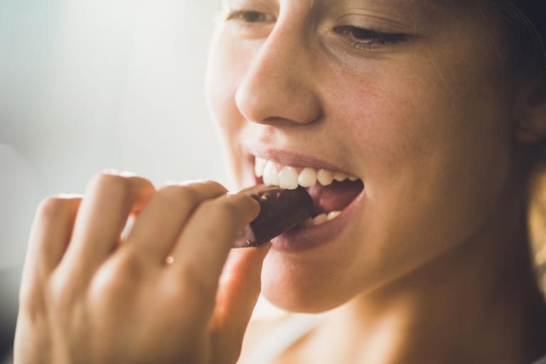 Frau beißt in Schokolade: Kakao ist gut für Herz-Kreislauf-Erkrankungen.