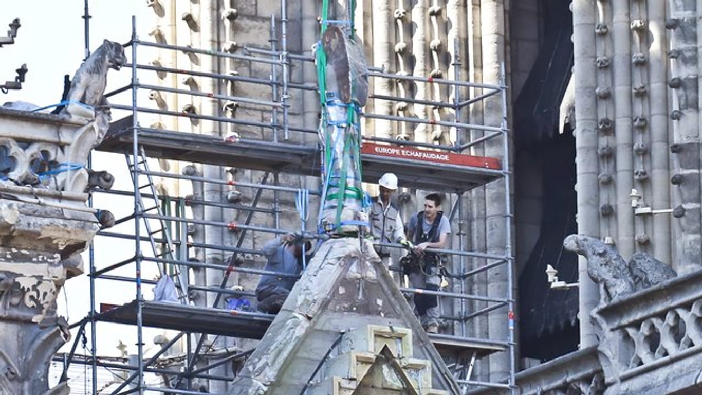 Arbeiter bereiten eine Statue auf einem Dach von Notre-Dame auf die Demontage durch einen Kran vor.