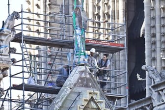 Arbeiter bereiten eine Statue auf einem Dach von Notre-Dame auf die Demontage durch einen Kran vor.