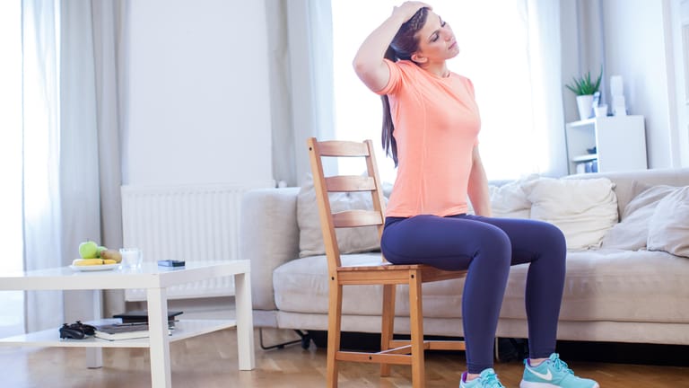 Frau macht Übung auf Stuhl: Gegen Verspannungen helfen oftmals Übungen, die man auch zuhause durchführen kann.