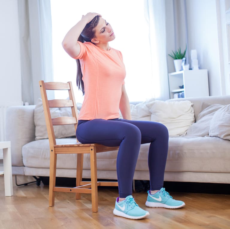 Frau macht Übung auf Stuhl: Gegen Verspannungen helfen oftmals Übungen, die man auch zuhause durchführen kann.