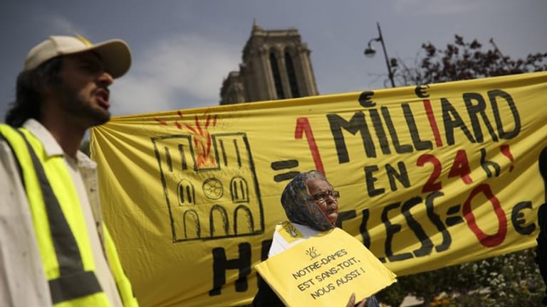 Bei einem Protest am Ostermontag vor der Notre-Dame Kathedrale werden Banner mit der Aufschrift auf Französisch: "Eine Milliarde in 24 Stunden! Obdachlos Null" und "Notre-Dame ist dachlos, wir auch!" gezeigt.