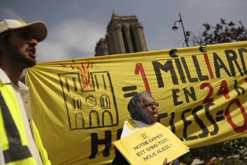 Bei einem Protest am Ostermontag vor der Notre-Dame Kathedrale werden Banner mit der Aufschrift auf Französisch: "Eine Milliarde in 24 Stunden! Obdachlos Null" und "Notre-Dame ist dachlos, wir auch!" gezeigt.
