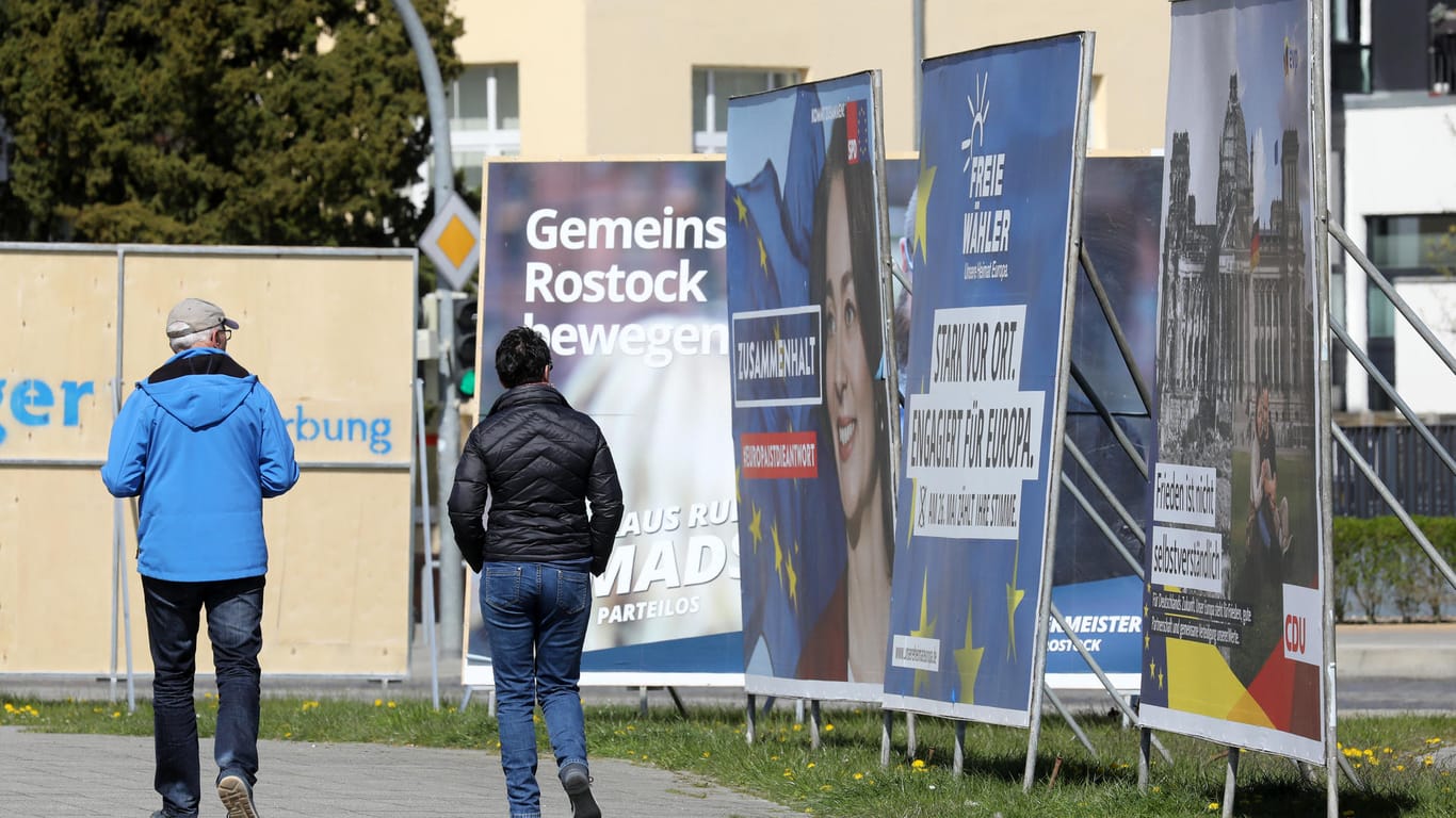 Passanten gehen in Rostock an Wahlplakaten der bevorstehenden Kommunal- und Europawahlen entlang
