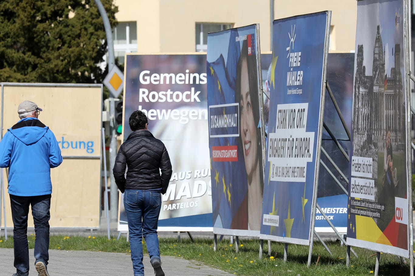 Passanten gehen in Rostock an Wahlplakaten der bevorstehenden Kommunal- und Europawahlen entlang