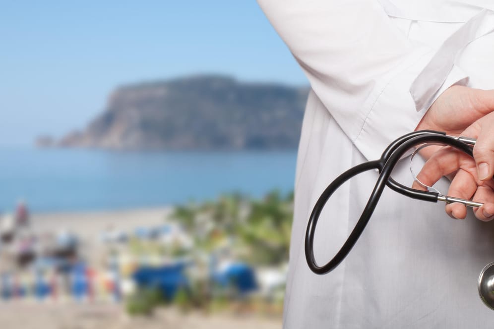Arzt blickt auf Strand: Für alle Reisen außerhalb Deutschlands sollten Urlauber eine Auslandskrankenversicherung in Betracht ziehen.