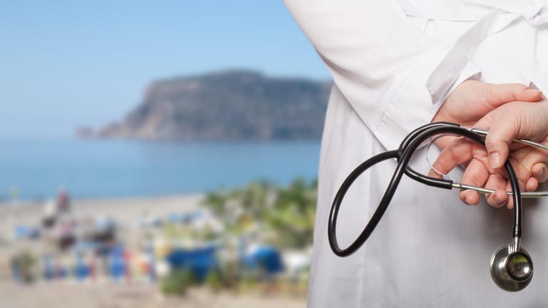 Arzt blickt auf Strand: Für alle Reisen außerhalb Deutschlands sollten Urlauber eine Auslandskrankenversicherung in Betracht ziehen.