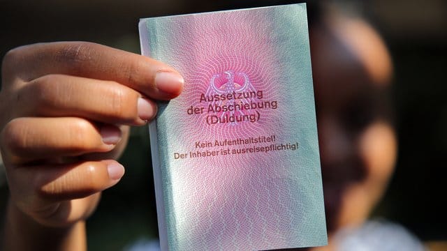 Eine junge Frau hält einen Ausweis für Flüchtlinge in der Hand mit dem Titel: Aussetzung der Abschiebung (Duldung).