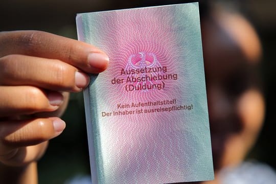 Eine junge Frau hält einen Ausweis für Flüchtlinge in der Hand mit dem Titel: Aussetzung der Abschiebung (Duldung).