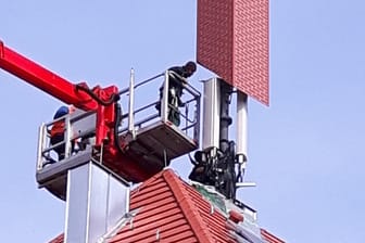 Ein Sendemast: Arbeiter verkleiden auf einem Wohn- und Geschäftshaus eine Mobilfunksendeanlage mit einer Schornsteinattrappe.