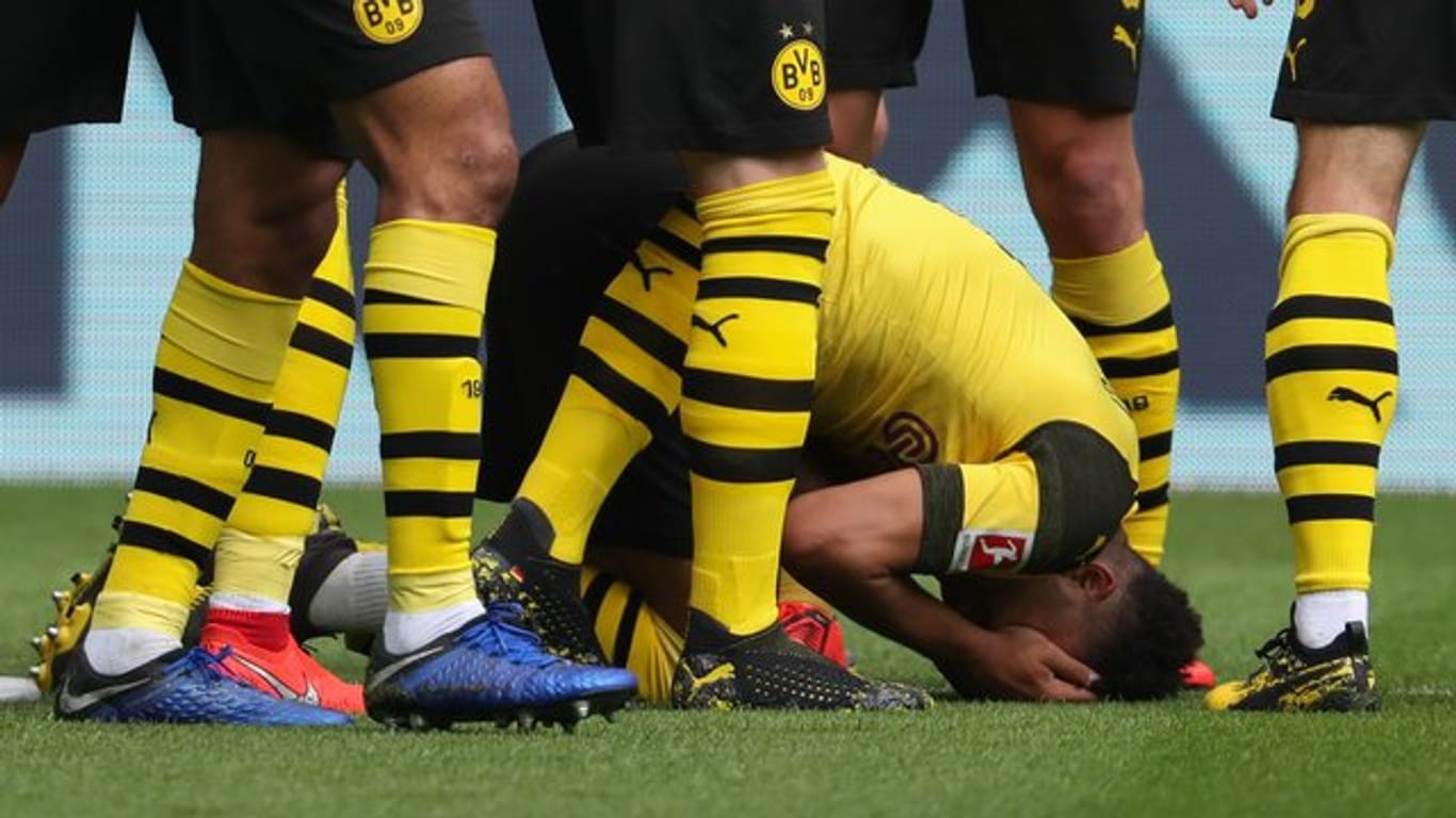 Der Dortmunder Jadon Sancho (unten) wurde von einem Feuerzeug aus der Schalker Kurve getroffen und kniet auf dem Rasen.