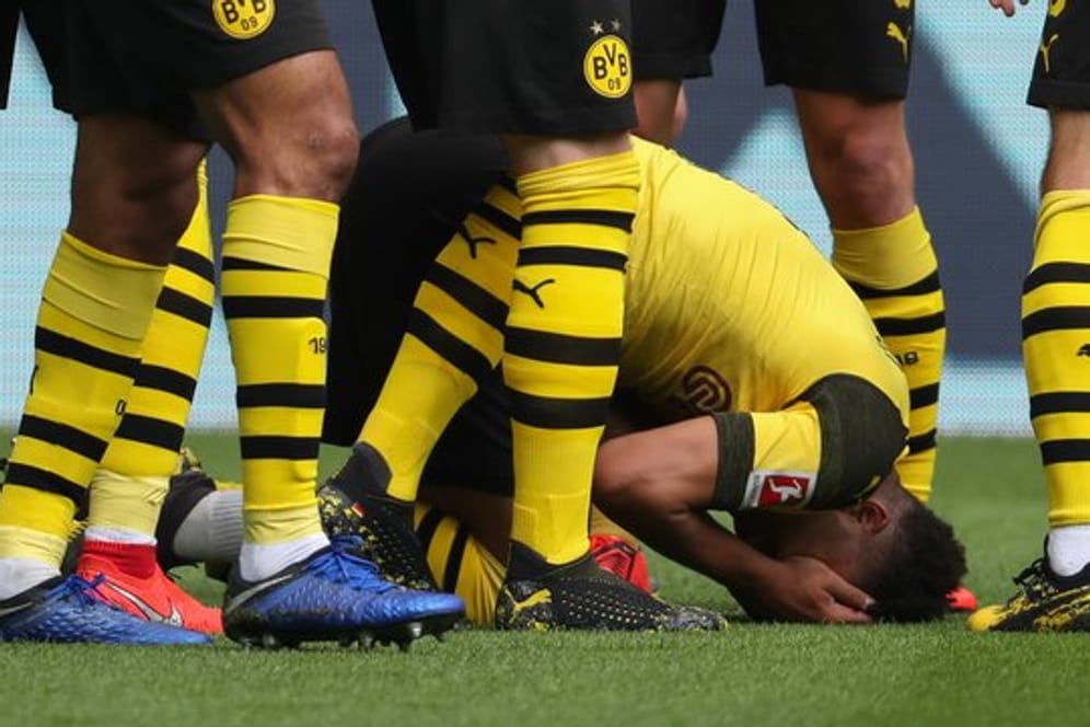 Der Dortmunder Jadon Sancho (unten) wurde von einem Feuerzeug aus der Schalker Kurve getroffen und kniet auf dem Rasen.