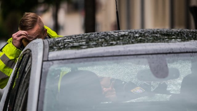 Zwei Polizeibeamte begutachten ein Fahrzeug mit beschädigter Heckscheibe im abgesperrten Bereich.