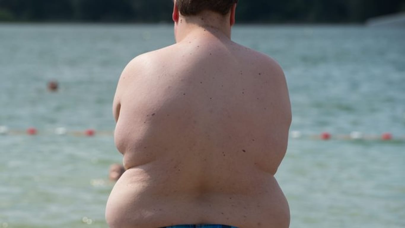 Ein übergewichtiger Junge steht an einem Badesee am Wasser.