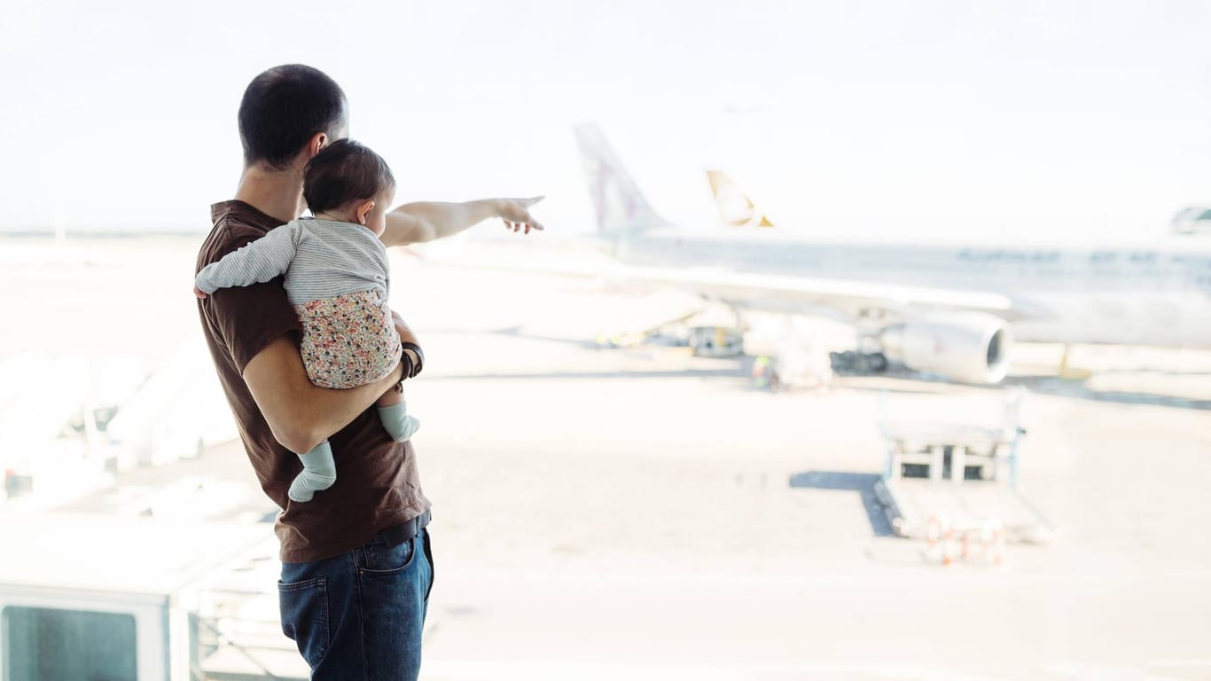 Mann mit Baby am Flughafen: In den ersten Lebensmonaten sollte abgewogen werden, ob eine Flugreise notwendig ist.