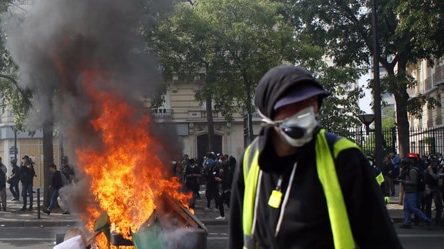 Ein Anhänger der "Gelbwesten" geht in Paris während einer Demonstration an brennenden Gegenständen vorbei.