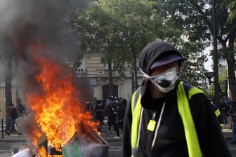Ein Anhänger der "Gelbwesten" geht in Paris während einer Demonstration an brennenden Gegenständen vorbei.