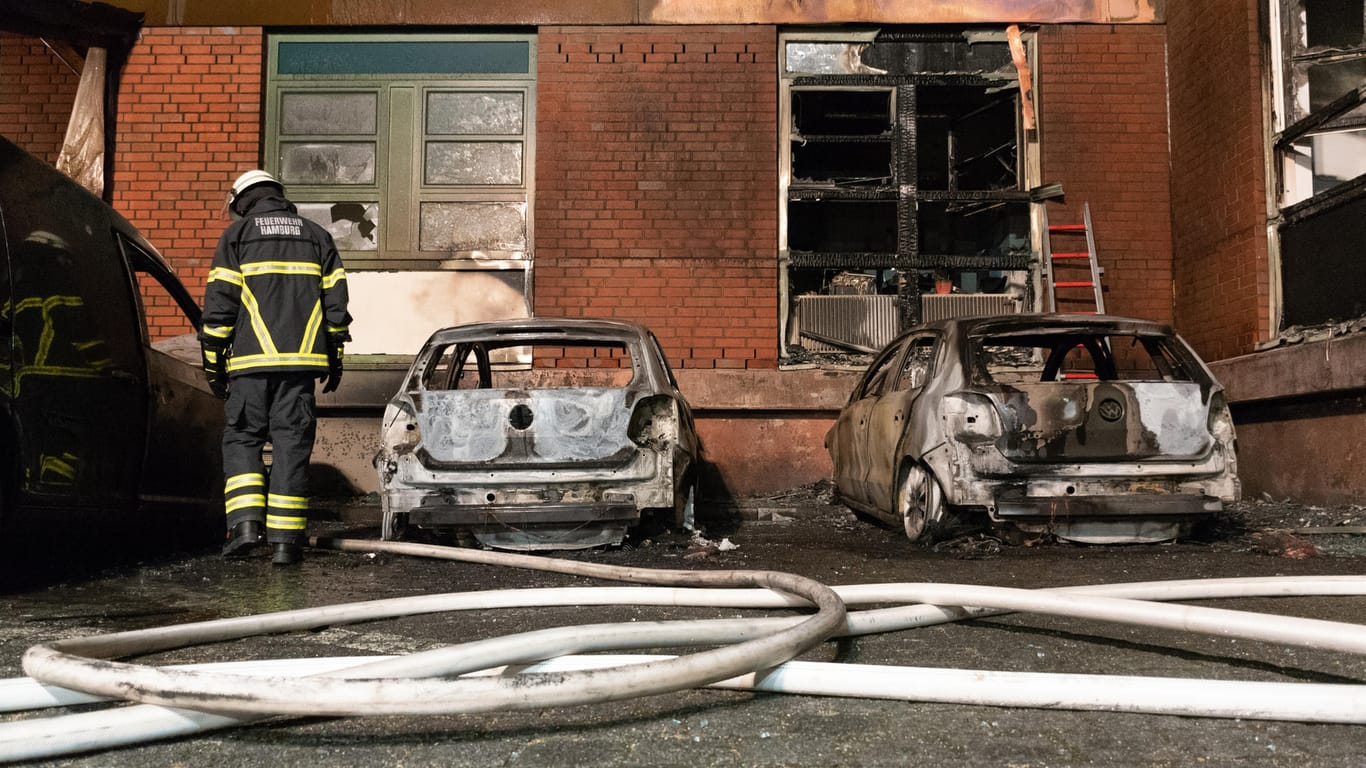 Ein Feuerwehrmann steht neben ausgebrannten Autos: Noch ist unklar, wer die Autos in Brand gesetzt hat.