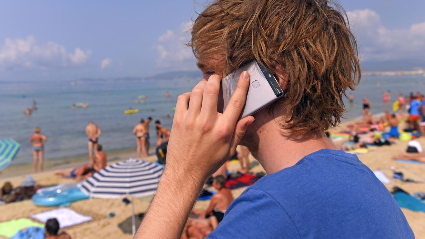 Ein junger Mann telefoniert am Strand von Mallorca: Dank der EU sind die Roaming-Gebühren im EU-Ausland Geschichte.