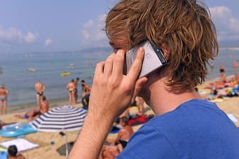 Ein junger Mann telefoniert am Strand von Mallorca: Dank der EU sind die Roaming-Gebühren im EU-Ausland Geschichte.