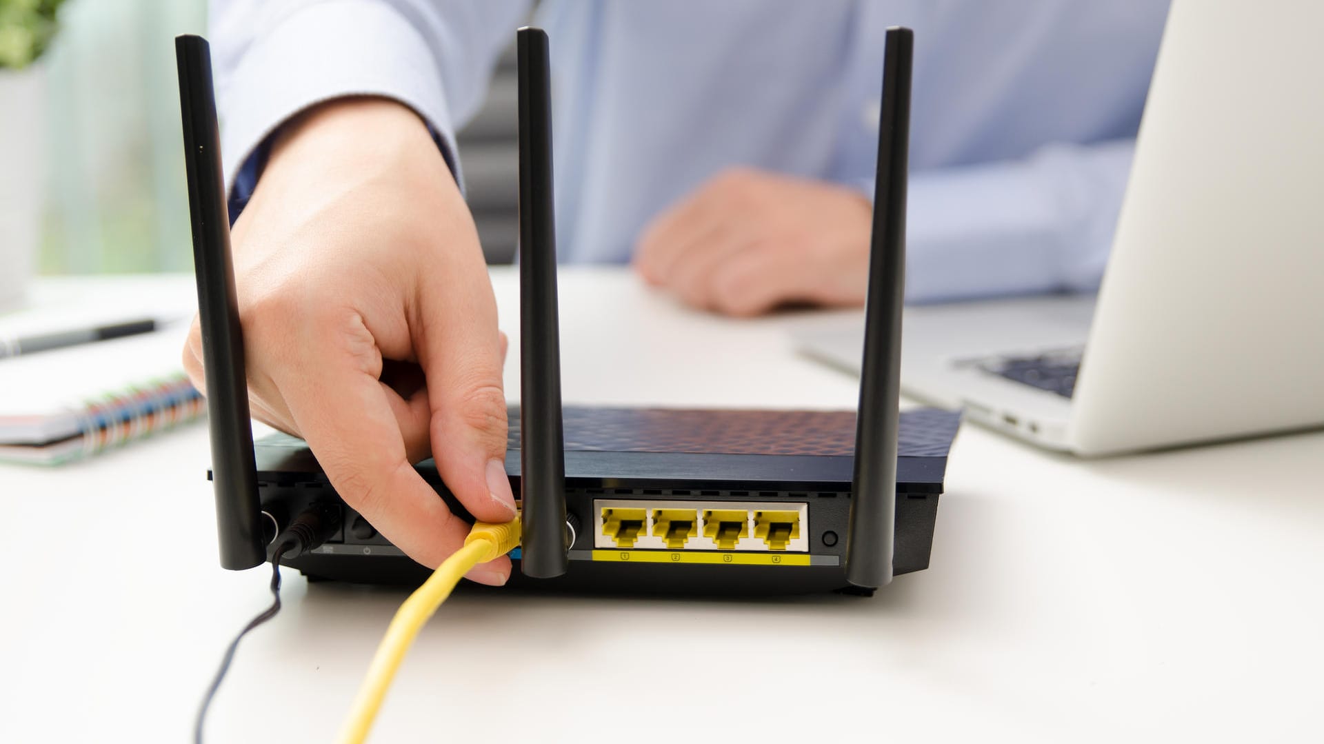 Ein Mann steckt ein Netzwerkkabel in den Router: Ein einfacher Test zeigt, ob der WLAN-Router gut abgesichert ist.