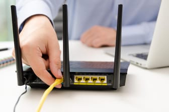 Ein Mann steckt ein Netzwerkkabel in den Router: Ein einfacher Test zeigt, ob der WLAN-Router gut abgesichert ist.