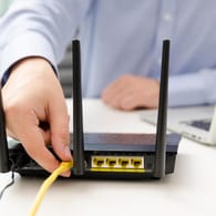 Ein Mann steckt ein Netzwerkkabel in den Router: Ein einfacher Test zeigt, ob der WLAN-Router gut abgesichert ist.