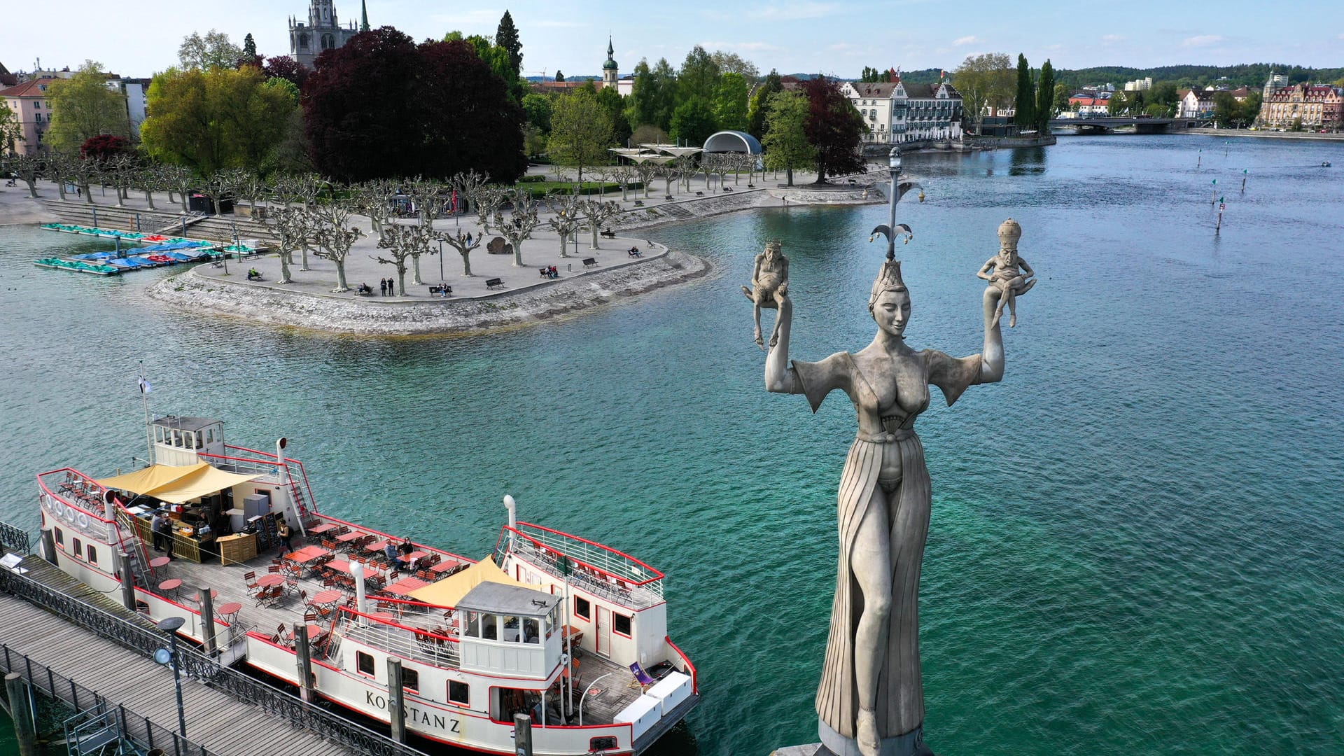 Die neun Meter hohe Statue Imperia, ein Kunstwerk von Bildhauer Peter Lenk, dreht sich an der Hafeneinfahrt von Konstanz am Bodensee neben dem historischen Fährschiff namens Konstanz.