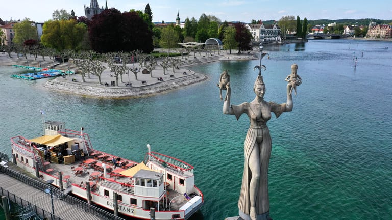 Die neun Meter hohe Statue Imperia, ein Kunstwerk von Bildhauer Peter Lenk, dreht sich an der Hafeneinfahrt von Konstanz am Bodensee neben dem historischen Fährschiff namens Konstanz.