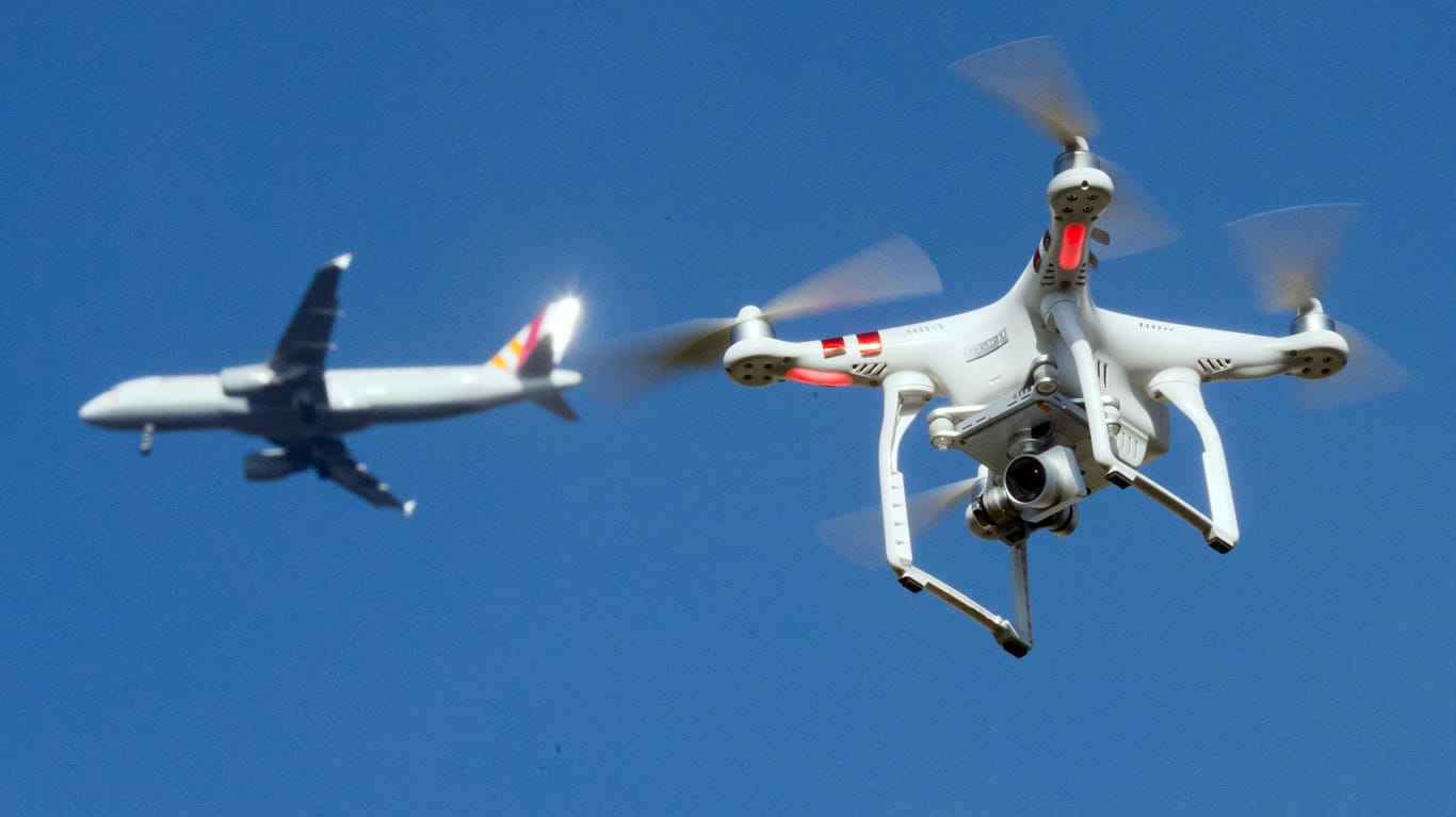 Eine private Drohne fliegt in knapp 10 Metern Flughöhe, als in weiter Entfernung ein Flugzeug beim Anflug auf einen Flughafen zu sehen ist (Symbolbild): Wegen einer Drohnensichtung ist der Betrieb am Frankfurter Flughafen schon am Donnerstag eingestellt worden.