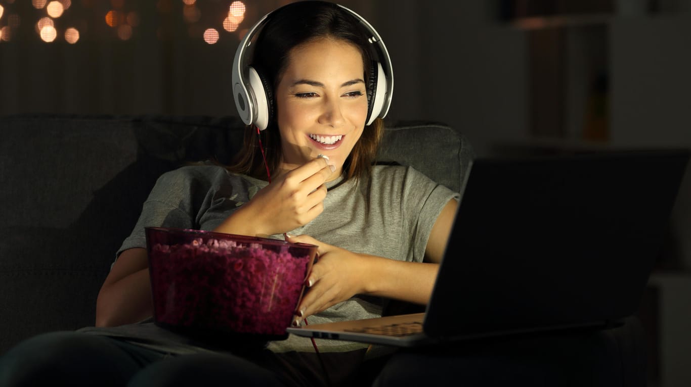 Eine Frau isst Popcorn, während sie einen Film auf dem Laptop schaut: Windows 10 hält ein paar tolle Funktionen für Filmfans parat.