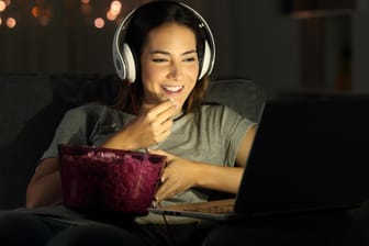 Eine Frau isst Popcorn, während sie einen Film auf dem Laptop schaut: Windows 10 hält ein paar tolle Funktionen für Filmfans parat.