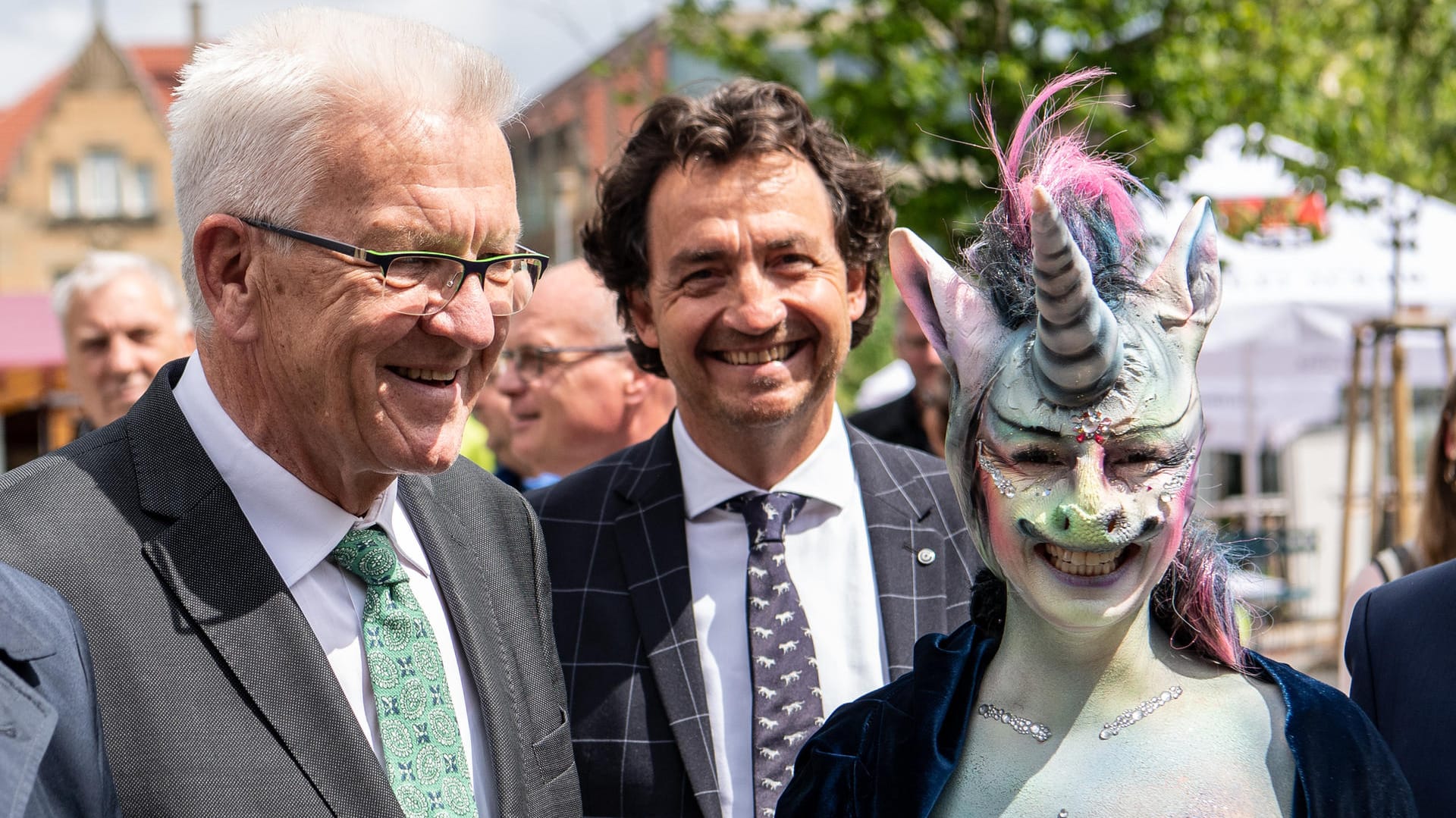 Winfried Kretschmann, Ministerpräsident von Baden-Württemberg, steht neben der als Einhorn maskierten Cynthia Schneider (Die Linke).