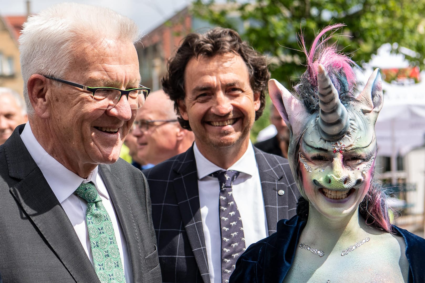 Winfried Kretschmann, Ministerpräsident von Baden-Württemberg, steht neben der als Einhorn maskierten Cynthia Schneider (Die Linke).