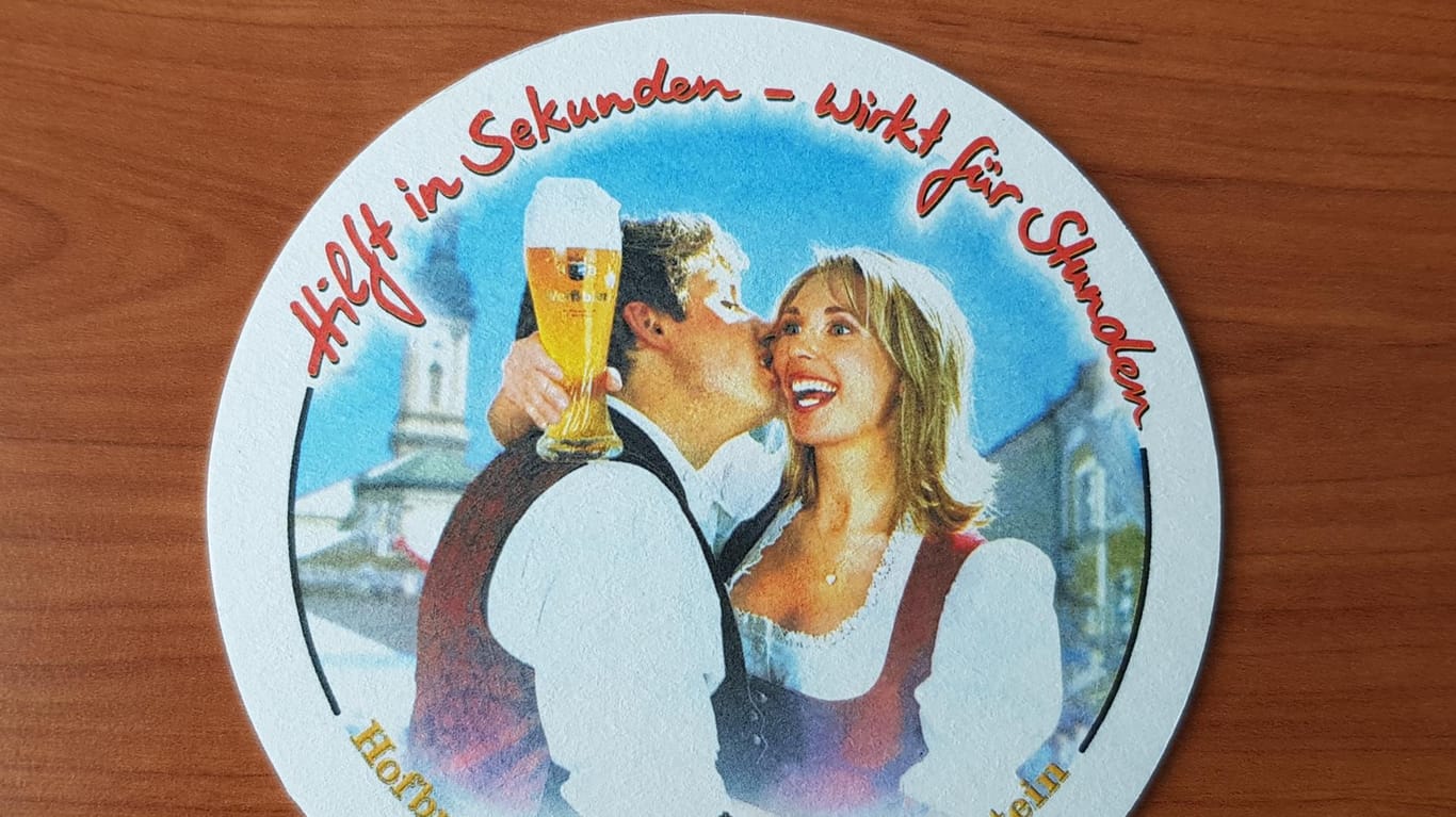 Ein Bierdeckel vom Hofbräuhaus Traunstein liegt auf einem Tisch: Der Brauereichef Maximilian Sailer gibt seiner Frau Brigitte einen Kuss und sie schaut auf ein volles Weißbierglas.