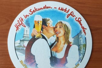 Ein Bierdeckel vom Hofbräuhaus Traunstein liegt auf einem Tisch: Der Brauereichef Maximilian Sailer gibt seiner Frau Brigitte einen Kuss und sie schaut auf ein volles Weißbierglas.