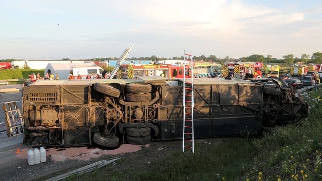 Einsatzkräfte der Feuerwehr stehen an der Unfallstelle neben dem verunglückten Bus. Einsatzkräfte der Feuerwehr stehen an der Unfallstelle neben dem verunglückten Bus.