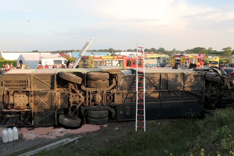 Einsatzkräfte der Feuerwehr stehen an der Unfallstelle neben dem verunglückten Bus.