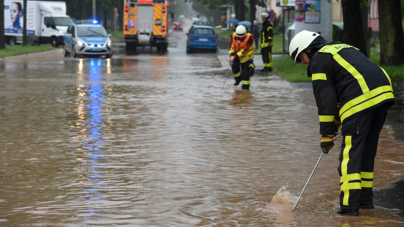 Regenmassen in Hessen: Feuerwehrleute suchen in Kassel mit Eisenstangen in einer überfluteten Straße nach dem Gullydeckel. Entwarnung gibt es noch nicht.