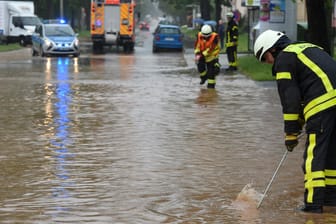 Regenmassen in Hessen: Feuerwehrleute suchen in Kassel mit Eisenstangen in einer überfluteten Straße nach dem Gullydeckel. Entwarnung gibt es noch nicht.
