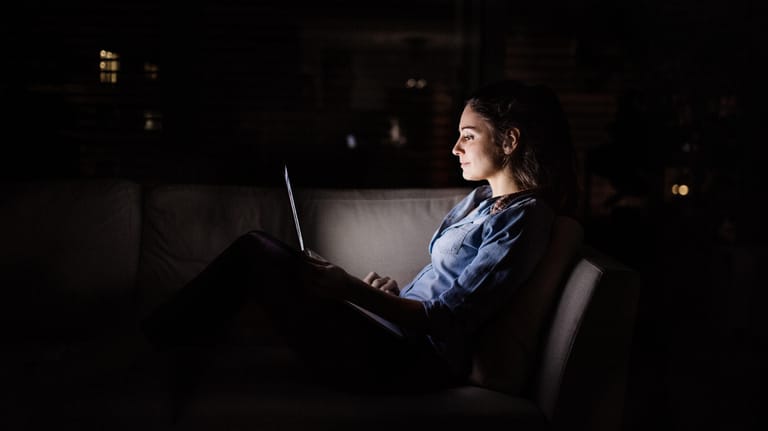 Eine Frau arbeitet im Dunkeln an ihrem Laptop: Der sogenannte "Dark Mode" schont in solchen Momenten die Augen.