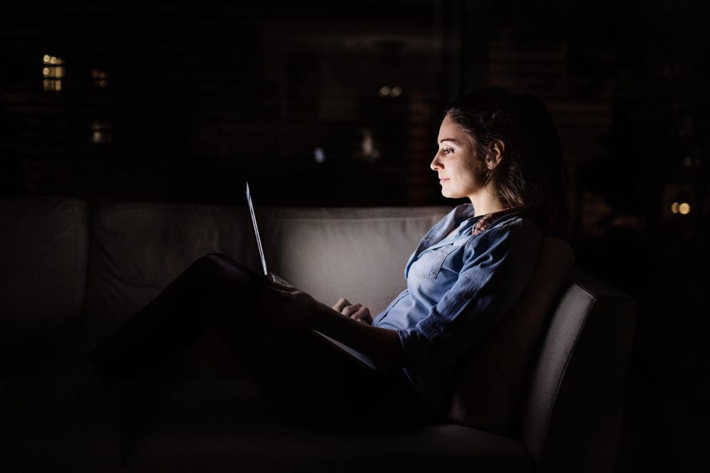 Eine Frau arbeitet im Dunkeln an ihrem Laptop: Der sogenannte "Dark Mode" schont in solchen Momenten die Augen.