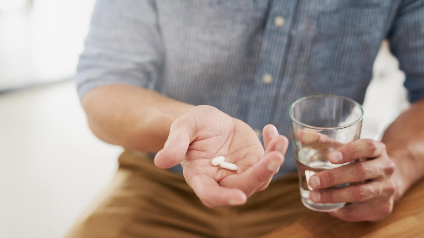 Mann hält Antibiotika und ein Glas Wasser in den Händen: Bei der Einnahme gibt es einiges zu beachten.