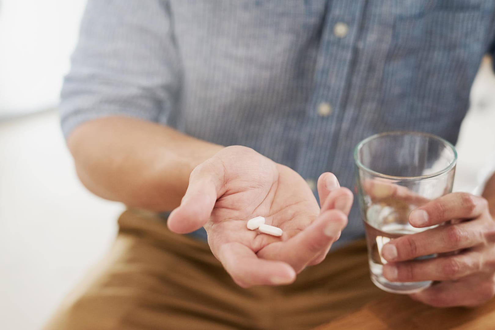 Mann hält Antibiotika und ein Glas Wasser in den Händen: Bei der Einnahme gibt es einiges zu beachten.