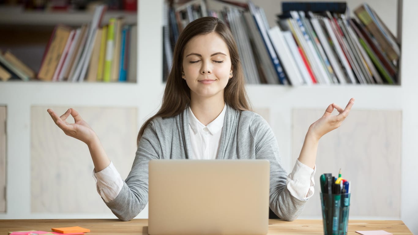 Frau meditiert vor einem Computer: Die Balance zwischen Arbeit und Freizeit zu finden, ist nicht immer leicht.