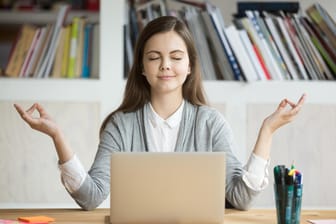 Frau meditiert vor einem Computer: Die Balance zwischen Arbeit und Freizeit zu finden, ist nicht immer leicht.