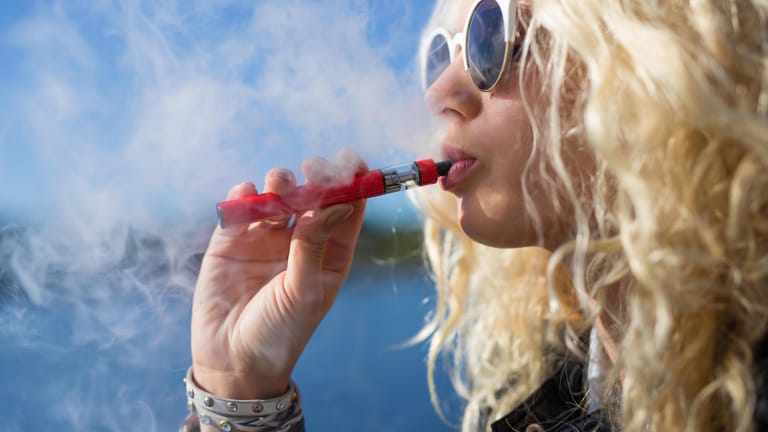 Frau inhaltiert Dampf aus einer E-Zigarette: Mediziner warnen vor schweren Folgen.